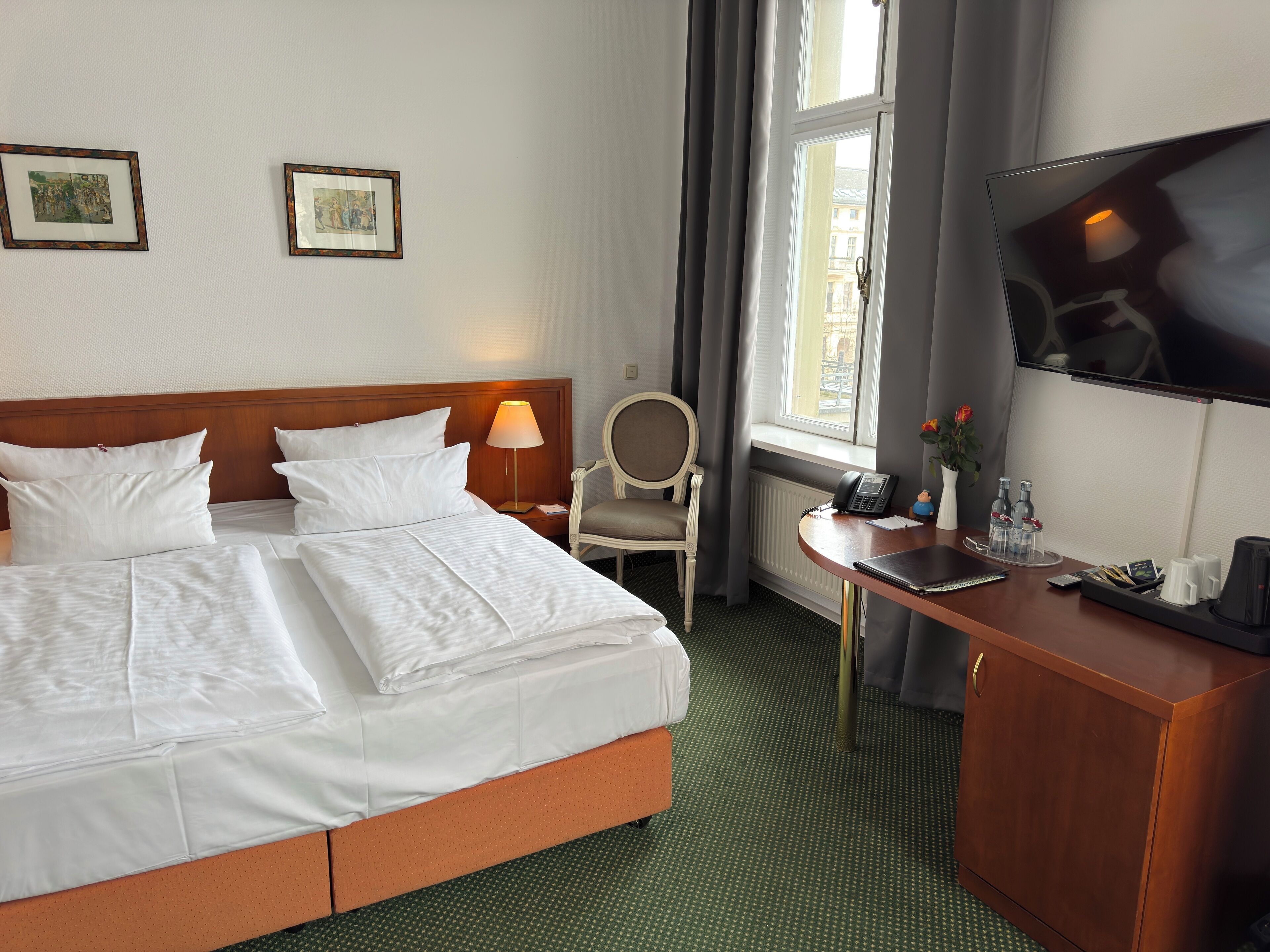 Una habitación de hotel con una cama grande, un escritorio con teléfono, una silla y un televisor en la pared.