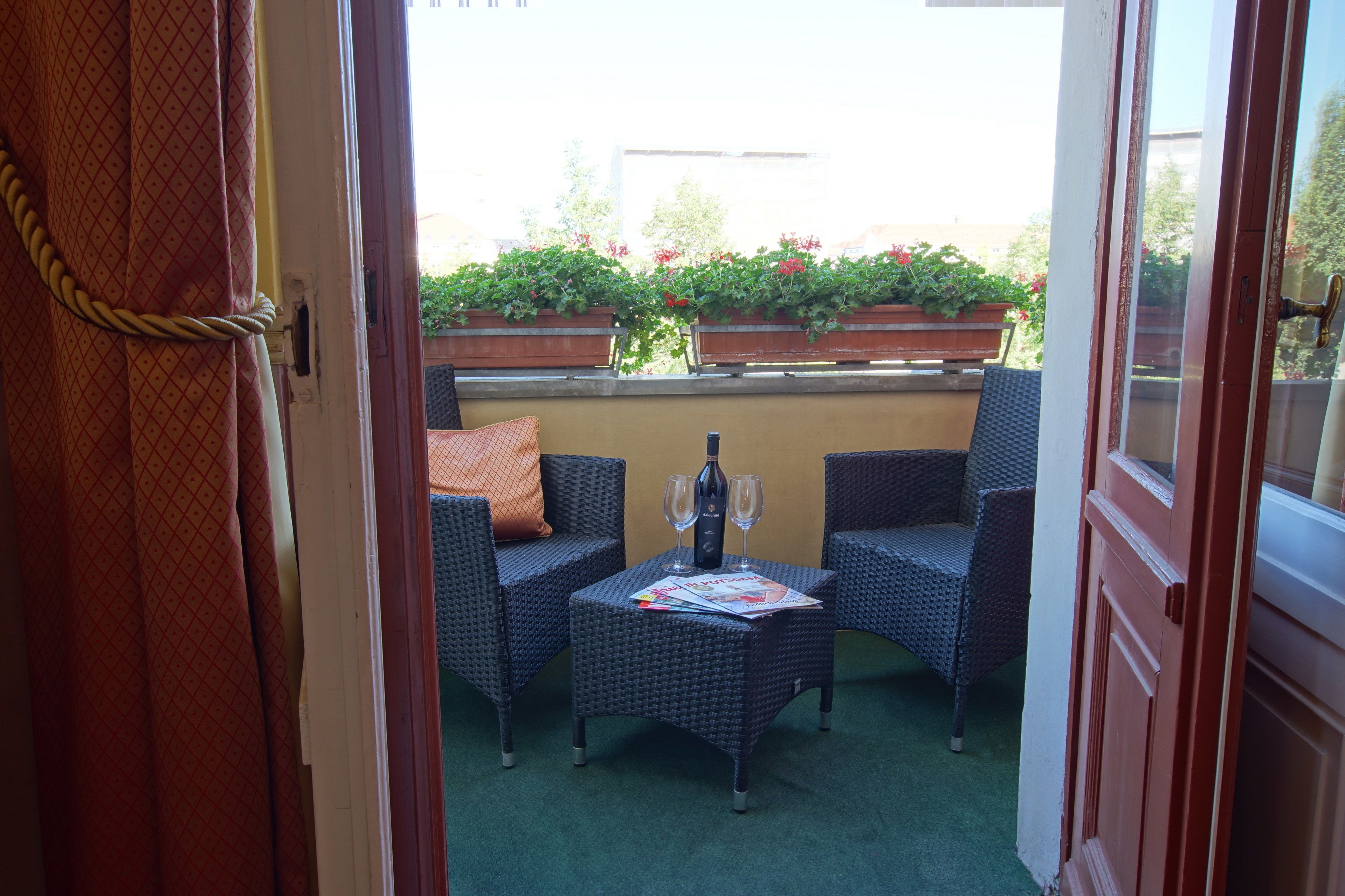 An open door to a balcony with wicker furniture, a bottle, and glasses.
