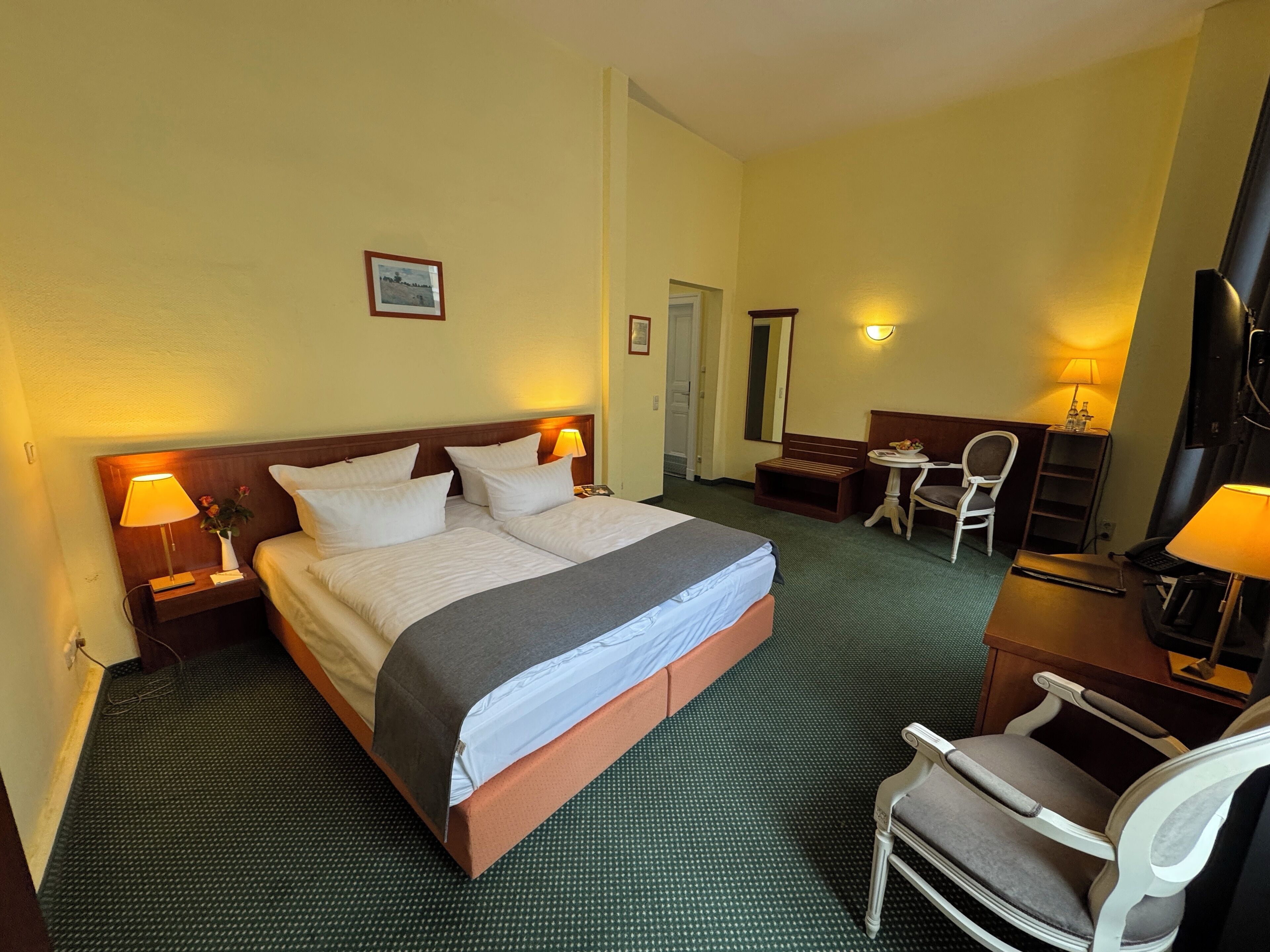 Habitación de hotel con una cama grande, dos mesitas de noche con lámparas, un escritorio con silla y una televisión.