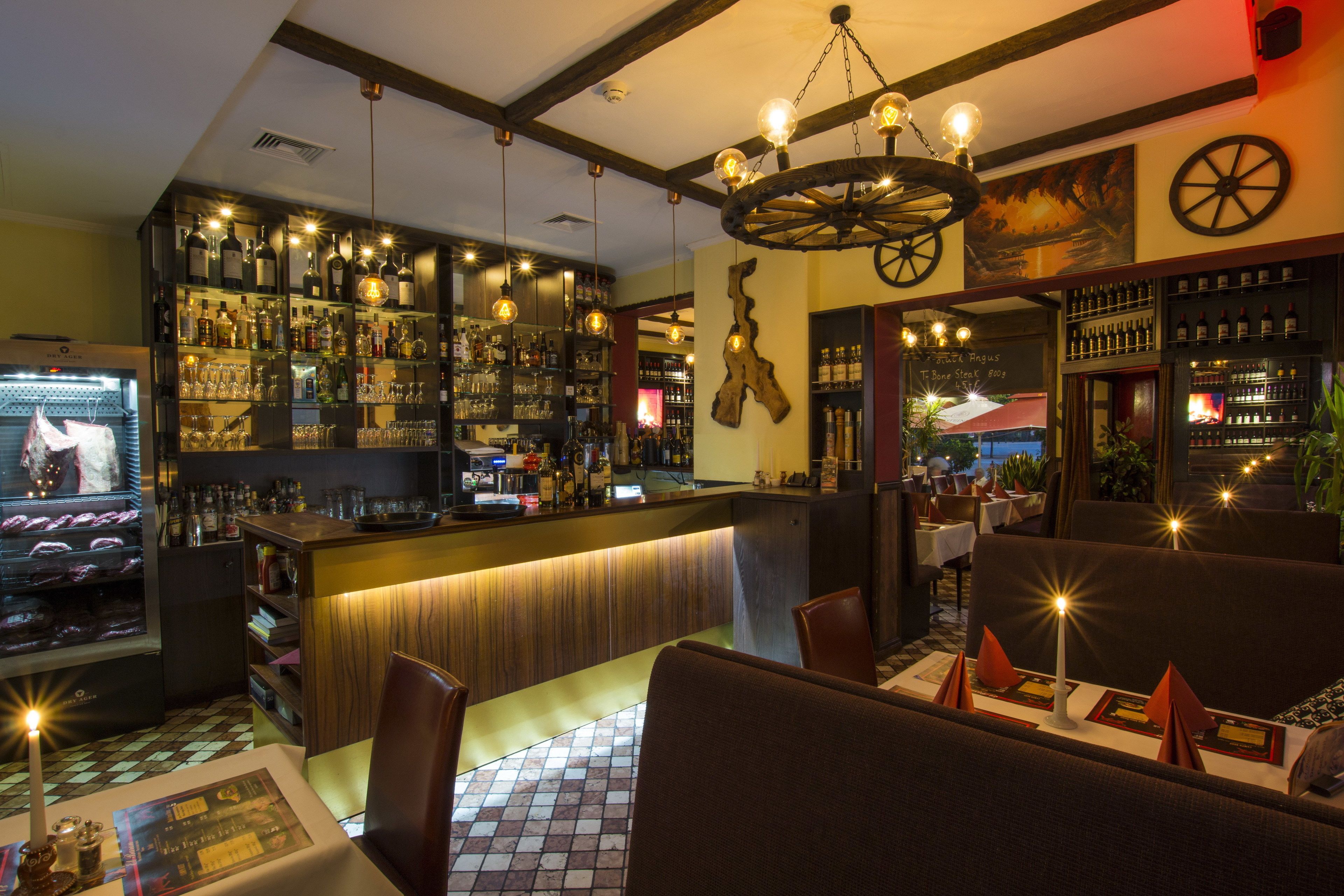 A bar area with a wooden counter, shelves of bottles, and hanging light fixtures.