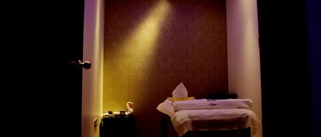 A dimly lit room with a bed, a nightstand, and a wall with a geometric pattern.