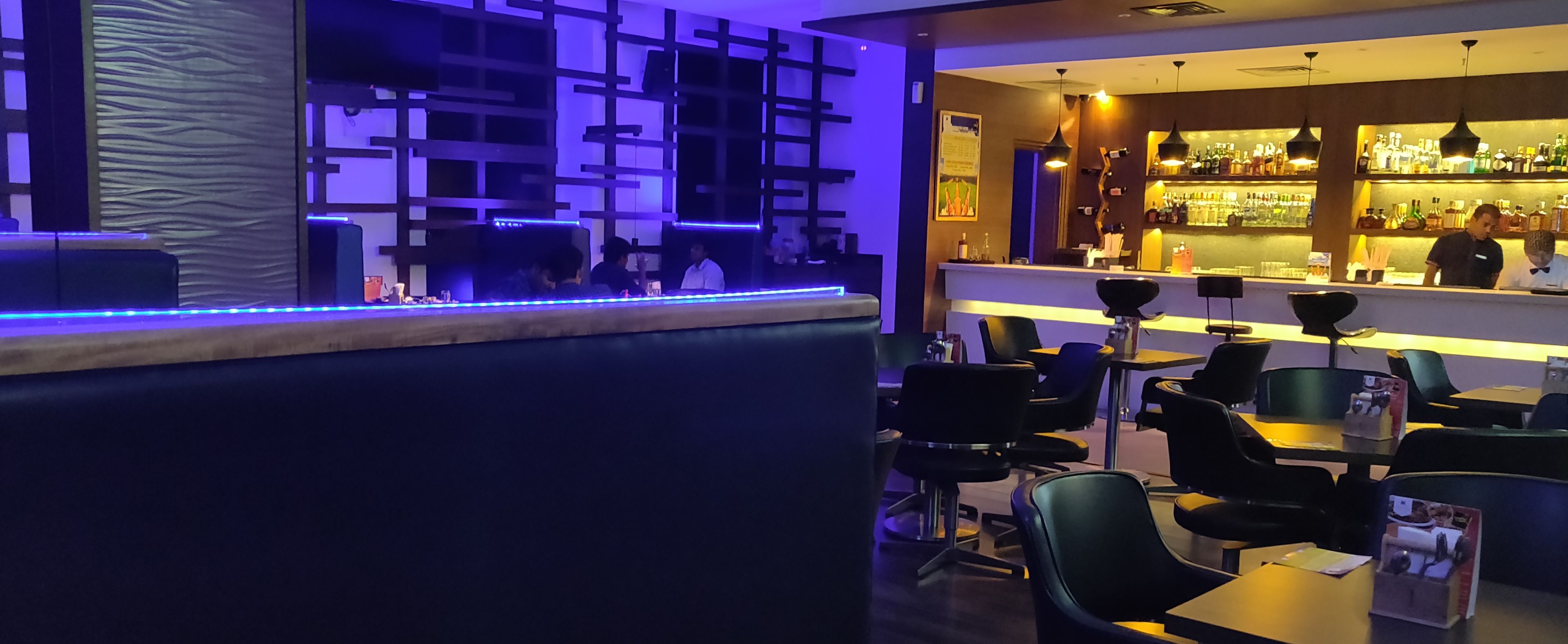 Zona de bar con barra, taburetes y un área de asientos con mesas y sillas.