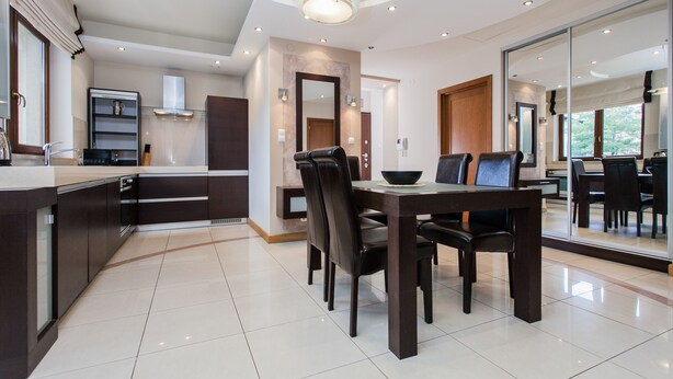 A modern kitchen with dark cabinetry, a dining area with a large table and chairs, and a large mirror reflecting the room. - Hamilton Suites - Atlantis Apartments (Krakow)