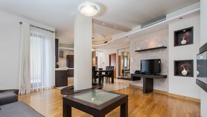 A modern living room with a glass-top coffee table, a sofa, and a TV on a stand. - Hamilton Suites - Atlantis Apartments (Krakow)