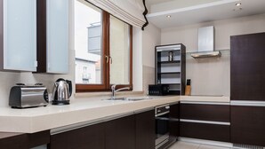 A modern kitchen with dark cabinetry, a stainless steel range hood, and a window with curtains. - Hamilton Suites - Atlantis Apartments (Krakow)