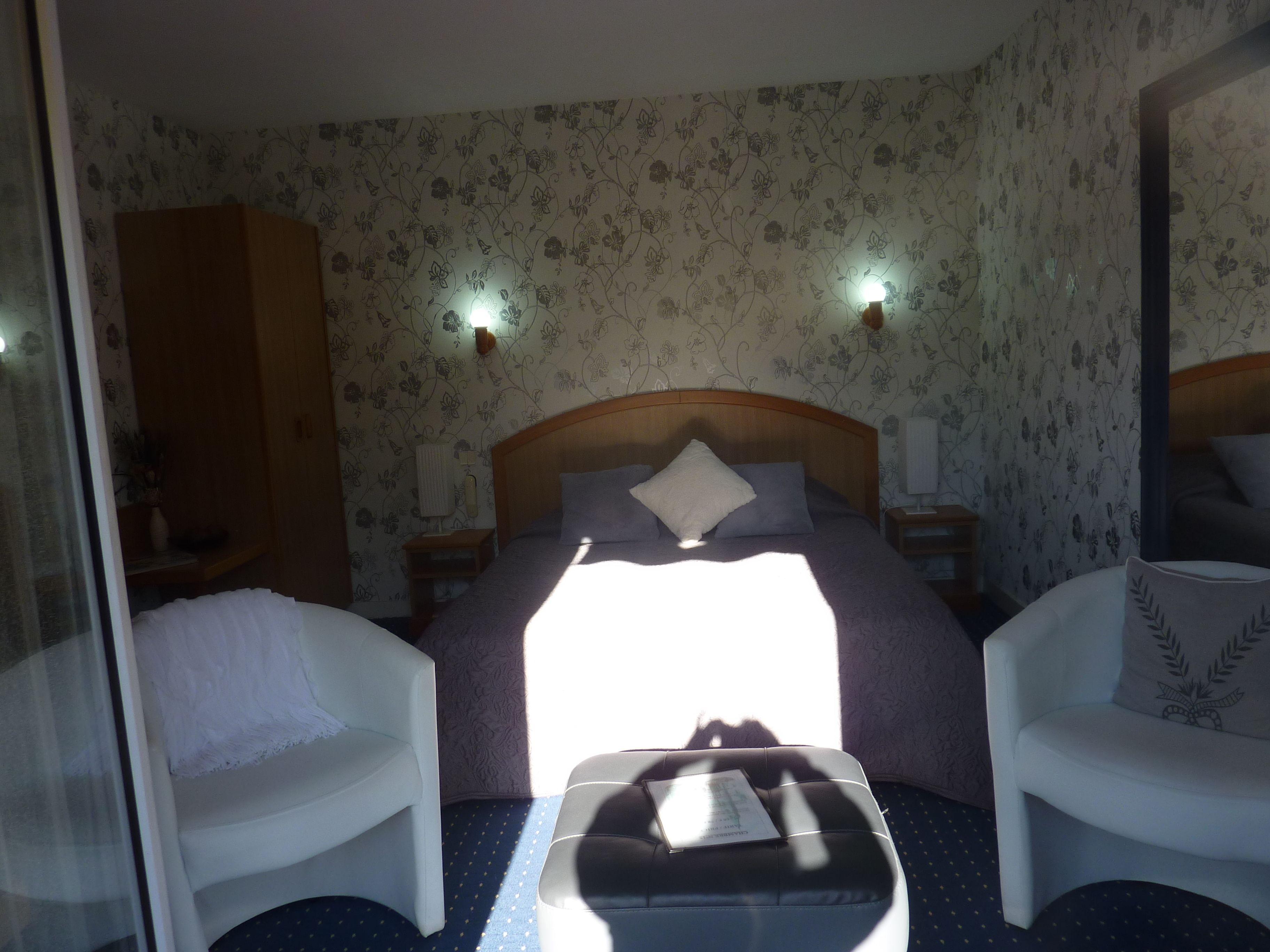 Une chambre d’hôtel avec un lit, deux tables de chevet, une petite table, une chaise, un canapé et une fenêtre laissant entrer la lumière du soleil.