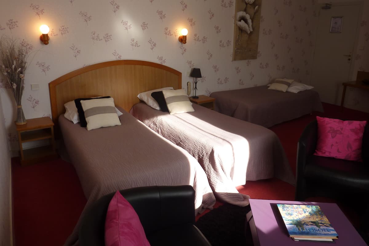 Hotellihuone, jossa on kaksi erillistä sänkyä, puinen pääty, yöpöytä lampun kanssa, pieni pöytä, jossa on kirja, ja tuoli, jossa on vaaleanpunainen koristetyyny.