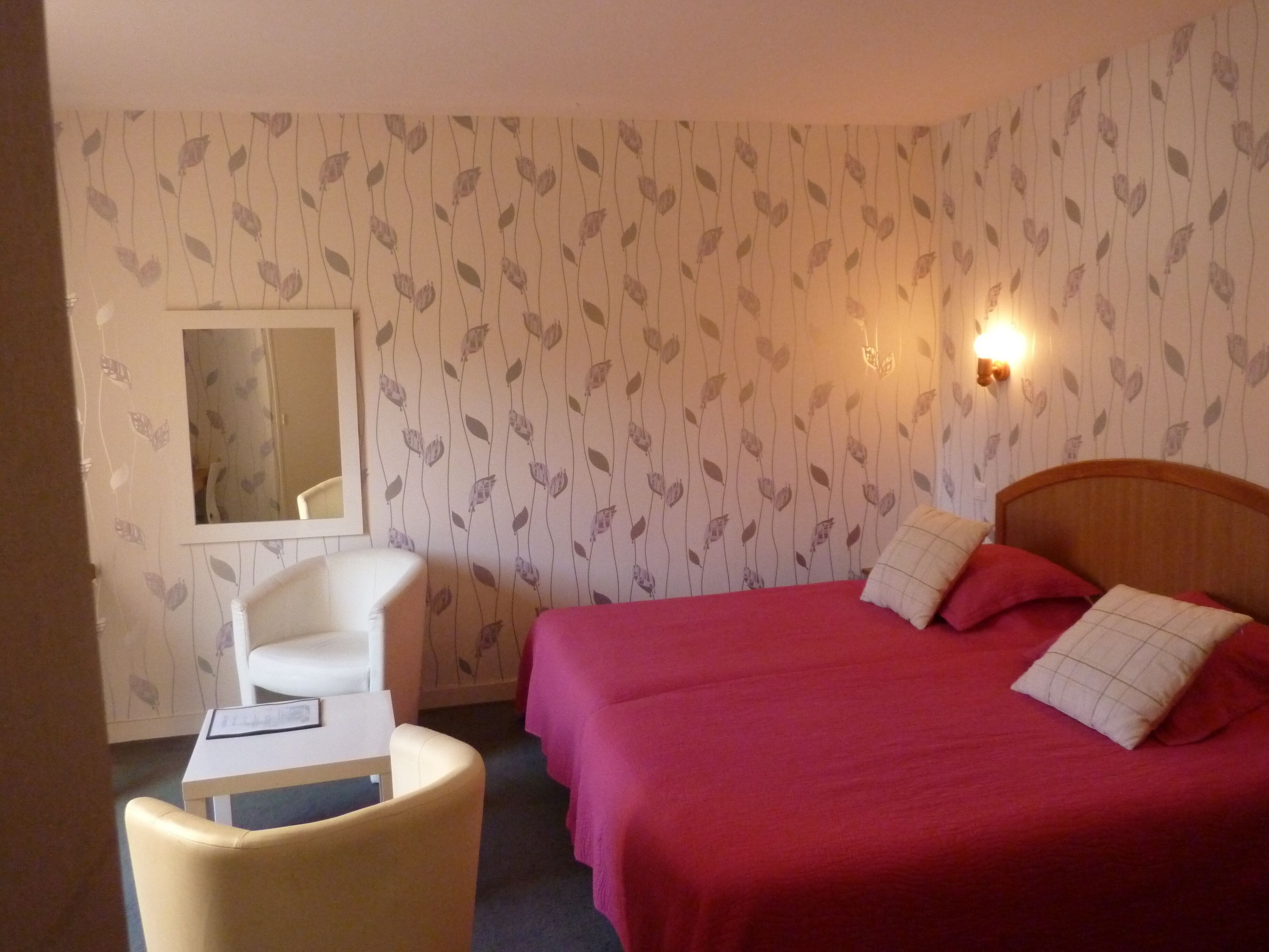 A hotel room with a bed, a chair, a small table, and a mirror.