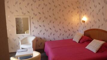 A hotel room with a bed, a chair, a small table, and a mirror.