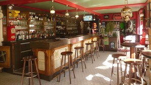 Eine Bar mit Holzhockern, einer Theke und Regalen voller Flaschen und Gläsern.