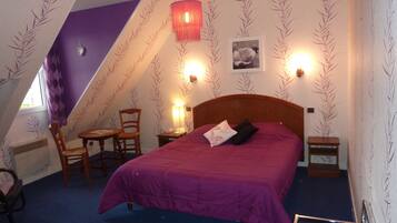 A bedroom with a bed, a chair, a small table, and a lamp.