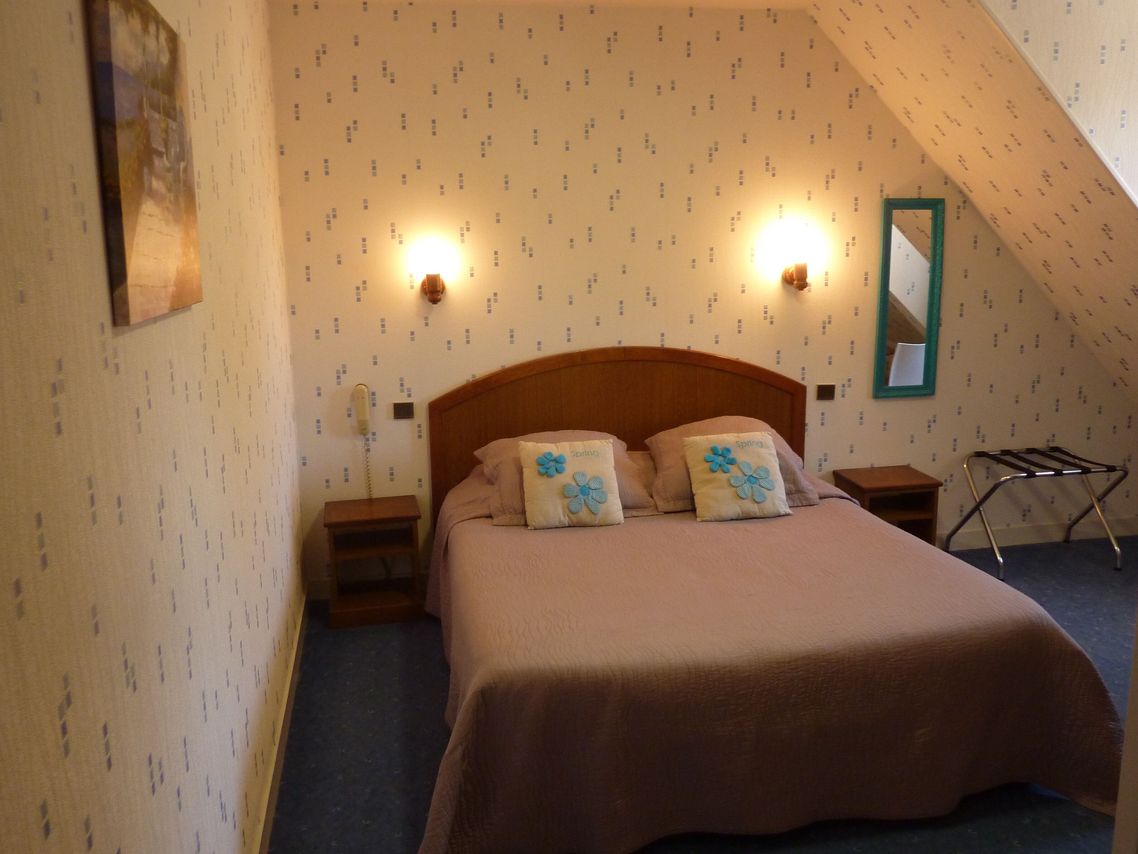 Un dormitorio con cabecera de madera, dos mesitas de noche, un teléfono de pared y un espejo.