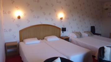 A hotel room with two single beds, a wooden headboard, a nightstand with a lamp, and floral wallpaper.