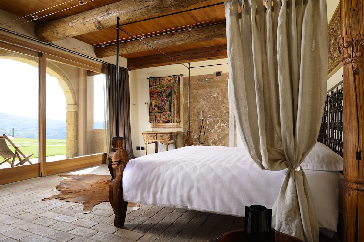 Un dormitorio con una cama grande, techo de madera, pared de piedra y vistas a través de un amplio ventanal.