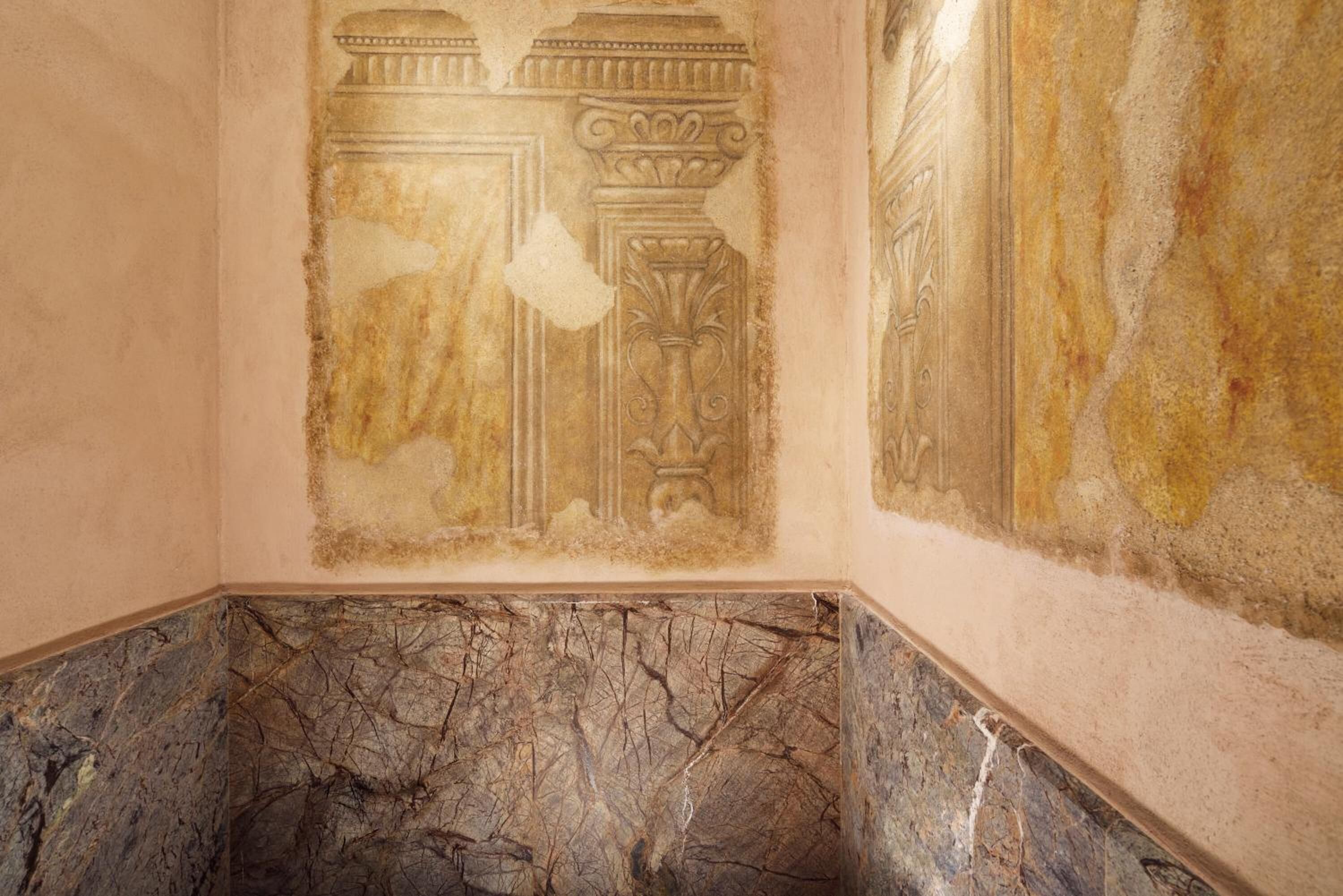 A room with a marble floor and a partially intact wall with classical architectural elements.