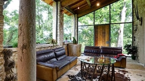 A rustic interior with stone pillars, leather sofas, a glass table, and a cowhide rug. - Tenuta Le Cave (Tregnago)