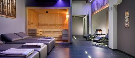A modern spa room with wooden sauna, massage beds, and a stone floor.