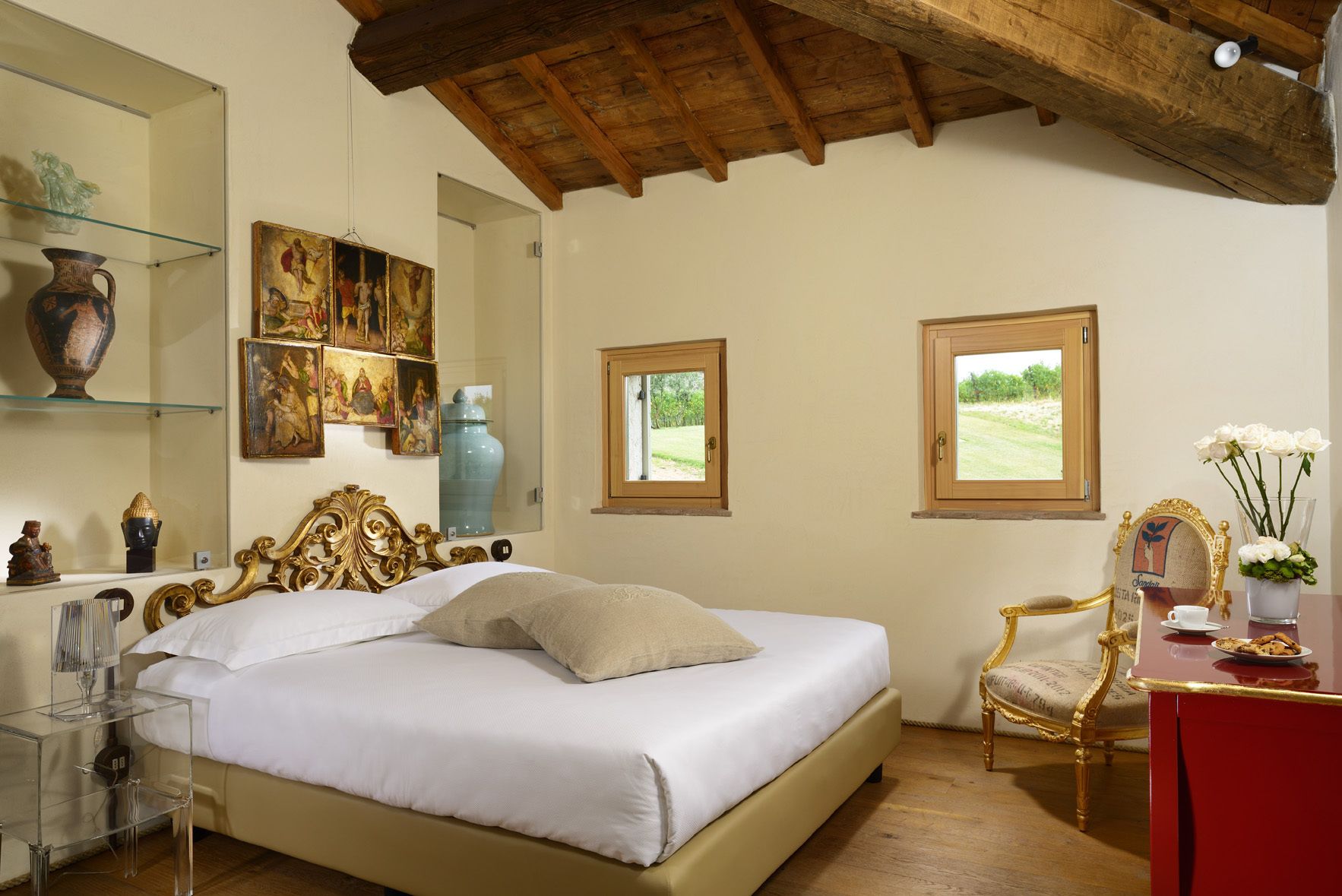 Une chambre dotée d’un grand lit, d’un plafond en bois, d’un bureau avec une chaise et de deux fenêtres donnant sur un paysage verdoyant.