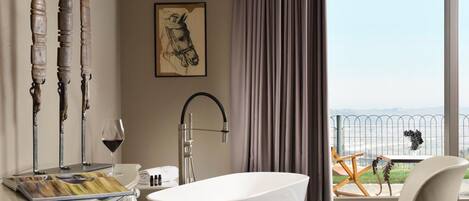A modern bathroom with a freestanding bathtub, a large window with a view, and a decorative wall piece.