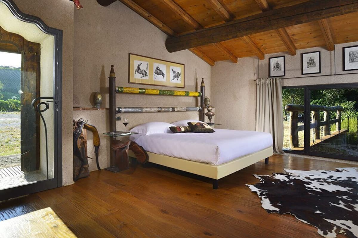 Un dormitorio con techo de madera, una cama con ropa blanca, una alfombra de cuero de vaca y cuadros en la pared.