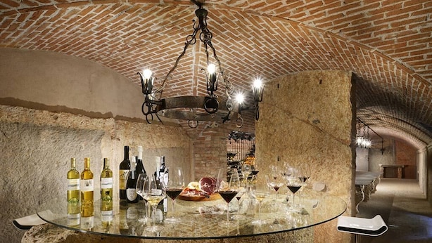 A bar with a glass table set with wine bottles and glasses, a chandelier, and stone walls. - Tenuta Le Cave (Tregnago)