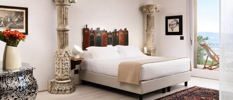 Un dormitorio con cama, mesita de noche, un jarrón con flores y dos columnas.