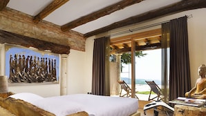 A bedroom with a large bed, wooden beams, a stone wall, a Buddha statue, and a view of the beach. - Tenuta Le Cave (Tregnago)