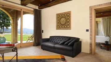A room with a black leather sofa, a large decorative wall piece, and a view of a green landscape through a glass door.