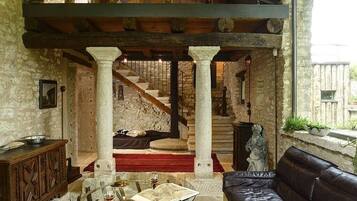 Un intérieur rustique avec des murs en pierre, un escalier en bois, un canapé en cuir et une table en verre sur laquelle reposent un livre et un verre à vin.