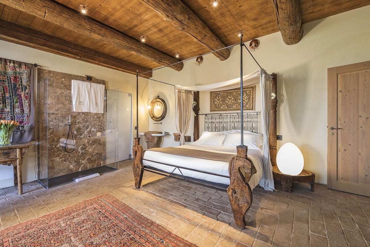 Un dormitorio con una cama grande, cabina de ducha de vidrio, techo de madera y decoración de estilo rústico.