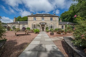 A stone building with a sign reading "Hotel" at the entrance, surrounded by a gravel path and picnic tables. - Bankton House Hotel (Livingston)