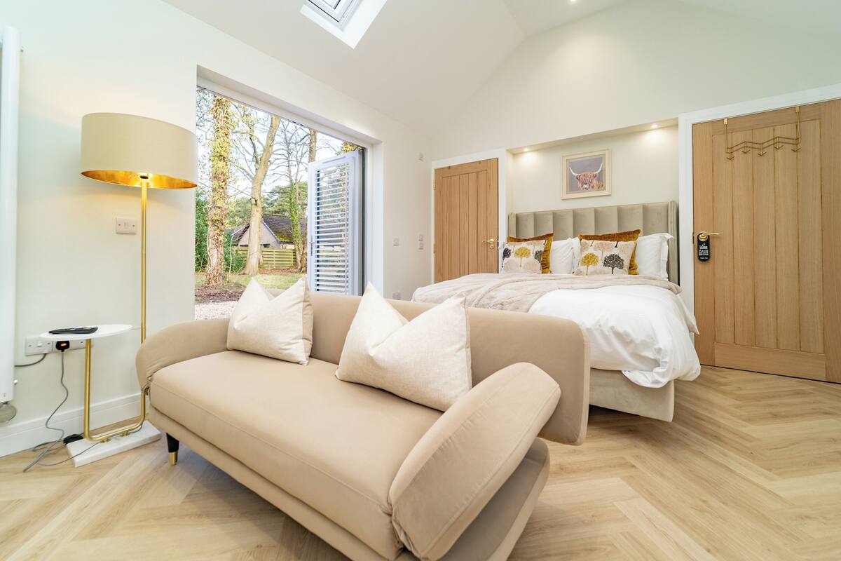 A modern bedroom with a bed, a sofa, a lamp, and a view of the outdoors.