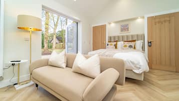 A modern bedroom with a bed, a sofa, a lamp, and a view of the outdoors.