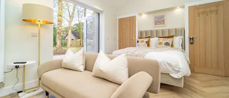 A modern bedroom with a bed, a sofa, a lamp, and a view of the outdoors.