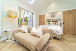 Ein modernes Schlafzimmer mit Bett, Sofa, Lampe und Blick ins Freie.