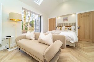 Un dormitorio moderno con cama, sofá, lámpara y vistas al exterior.