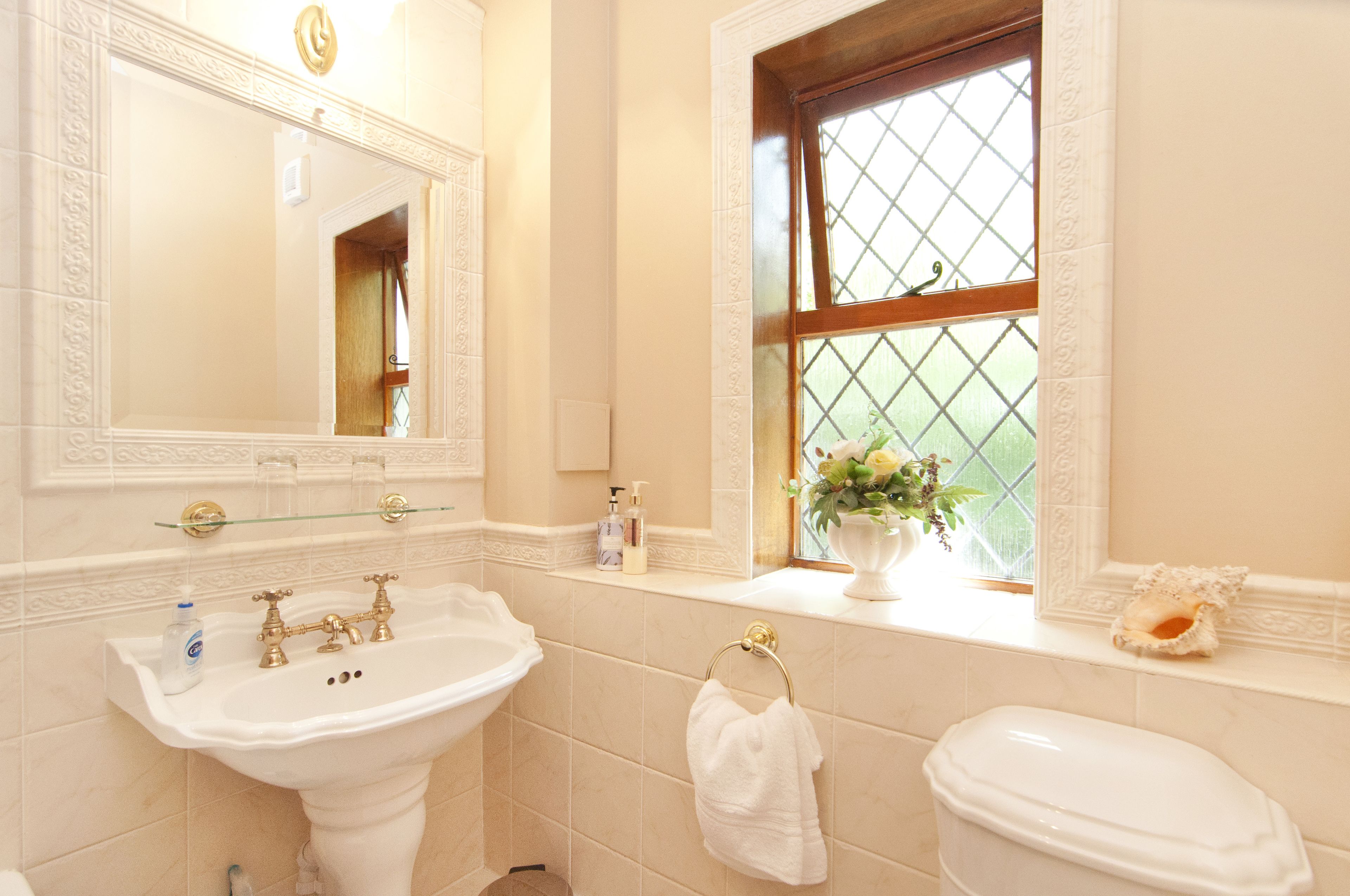 Een badkamer met een wit wastafelmeubel, een spiegel, een toilet en een raam met uitzicht op groen.