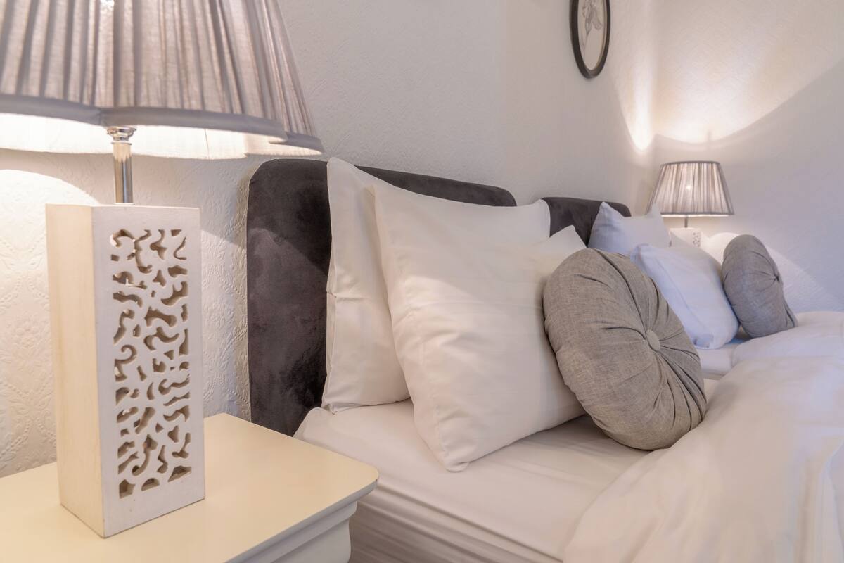 A neatly arranged bedroom with a bed, pillows, a bedside table, and a lamp.