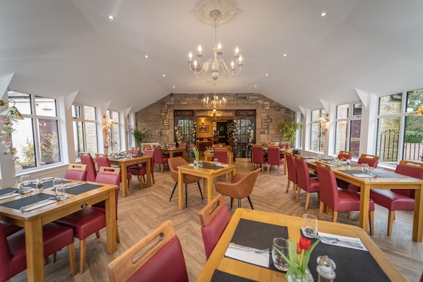 A spacious dining area with multiple tables and chairs, a chandelier, and large windows. - Bankton House and Lodges (Livingston)
