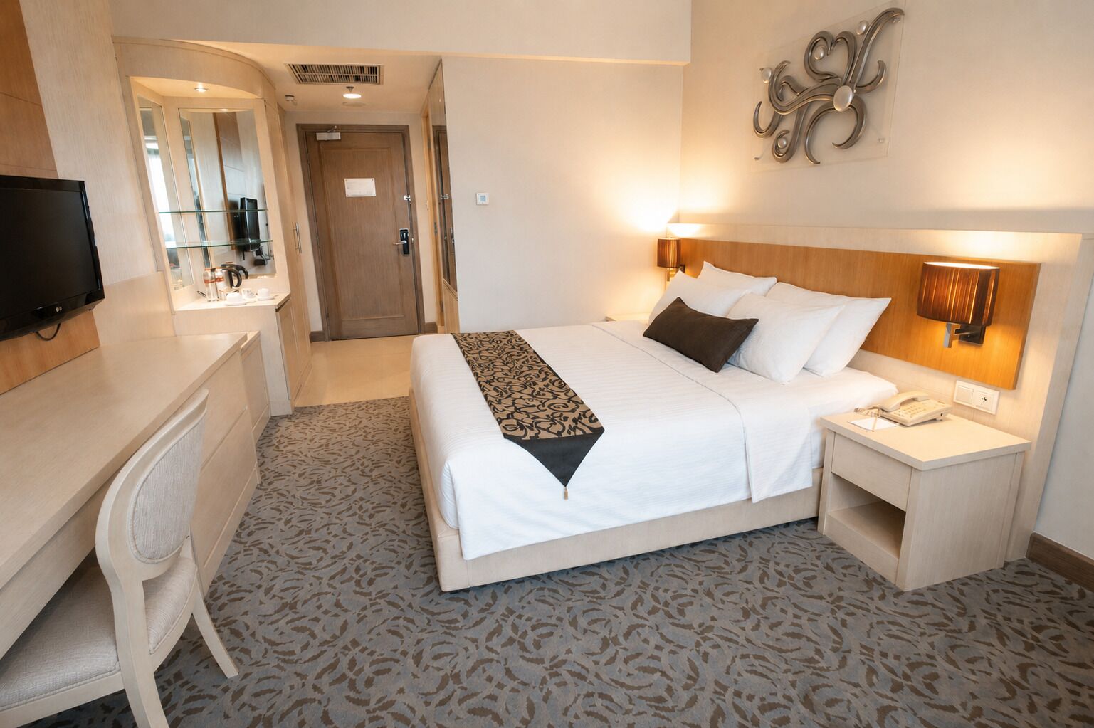 Ein Hotelzimmer mit Bett, Nachttisch, Lampe, Schreibtisch, Stuhl und Fernseher.