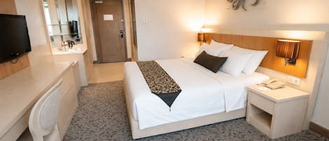 Ein Hotelzimmer mit Bett, Nachttisch, Lampe, Schreibtisch, Stuhl und Fernseher.