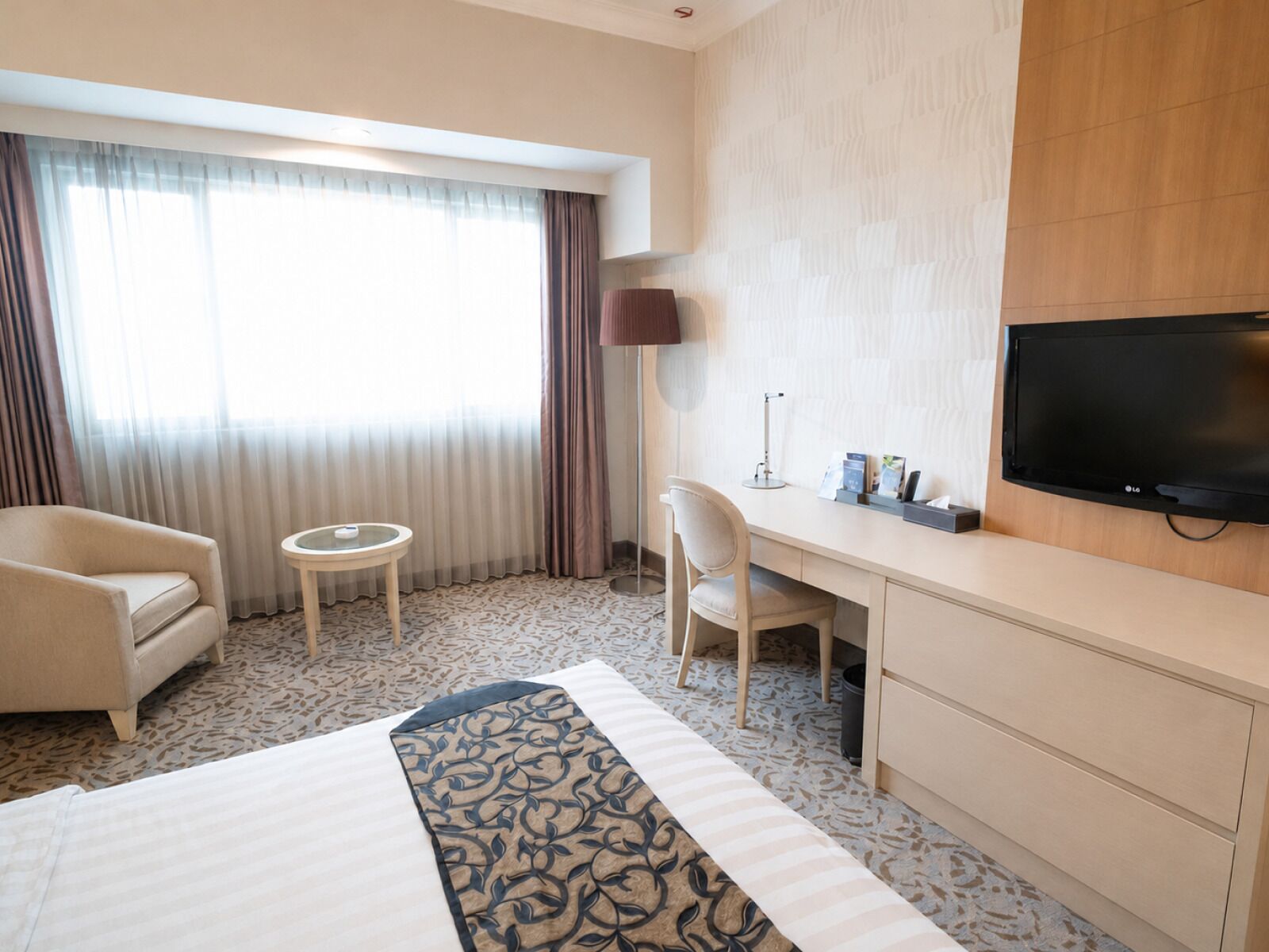 A hotel room with a bed, a desk, a chair, a television, and a window with curtains.