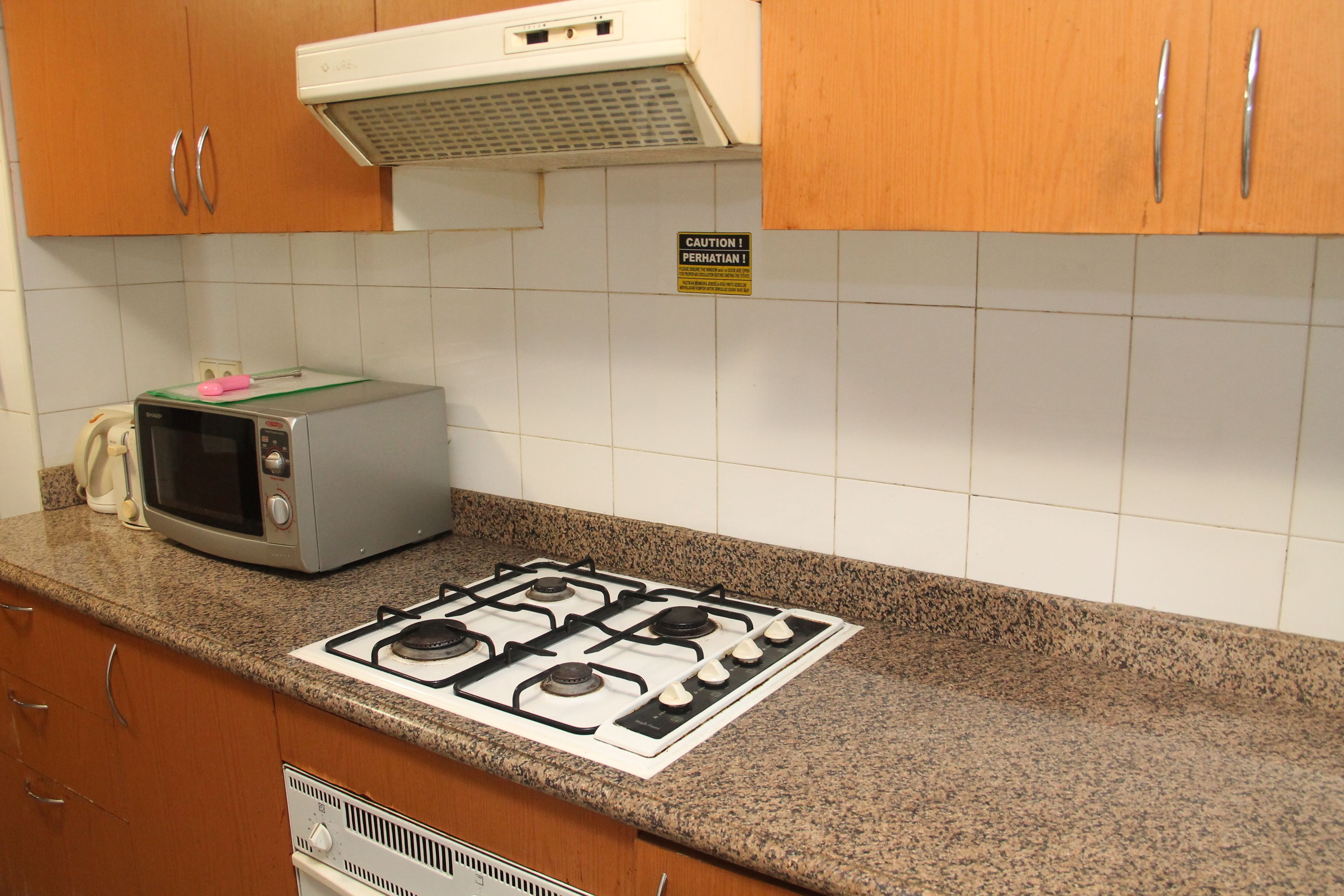 A kitchen with a microwave, stove, and a caution sign on the wall.
