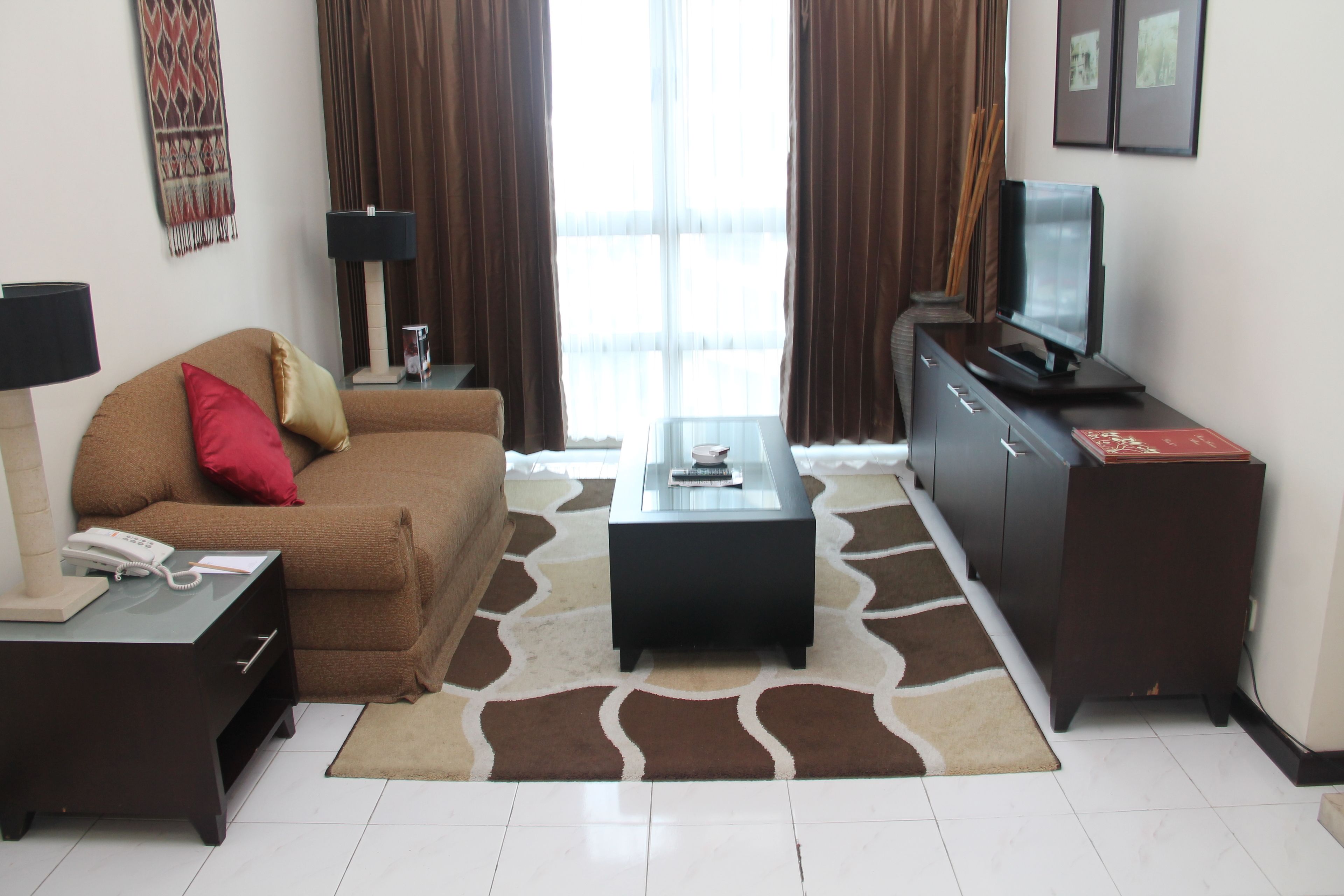 A living room with a brown sofa, a glass coffee table, a dark wooden TV stand, and a patterned rug.