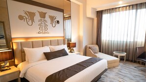 Une chambre d’hôtel avec un grand lit, une chaise, une petite table et un élément décoratif mural.