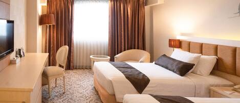 A hotel room with a bed, a desk, a chair, a television, and a window with curtains.