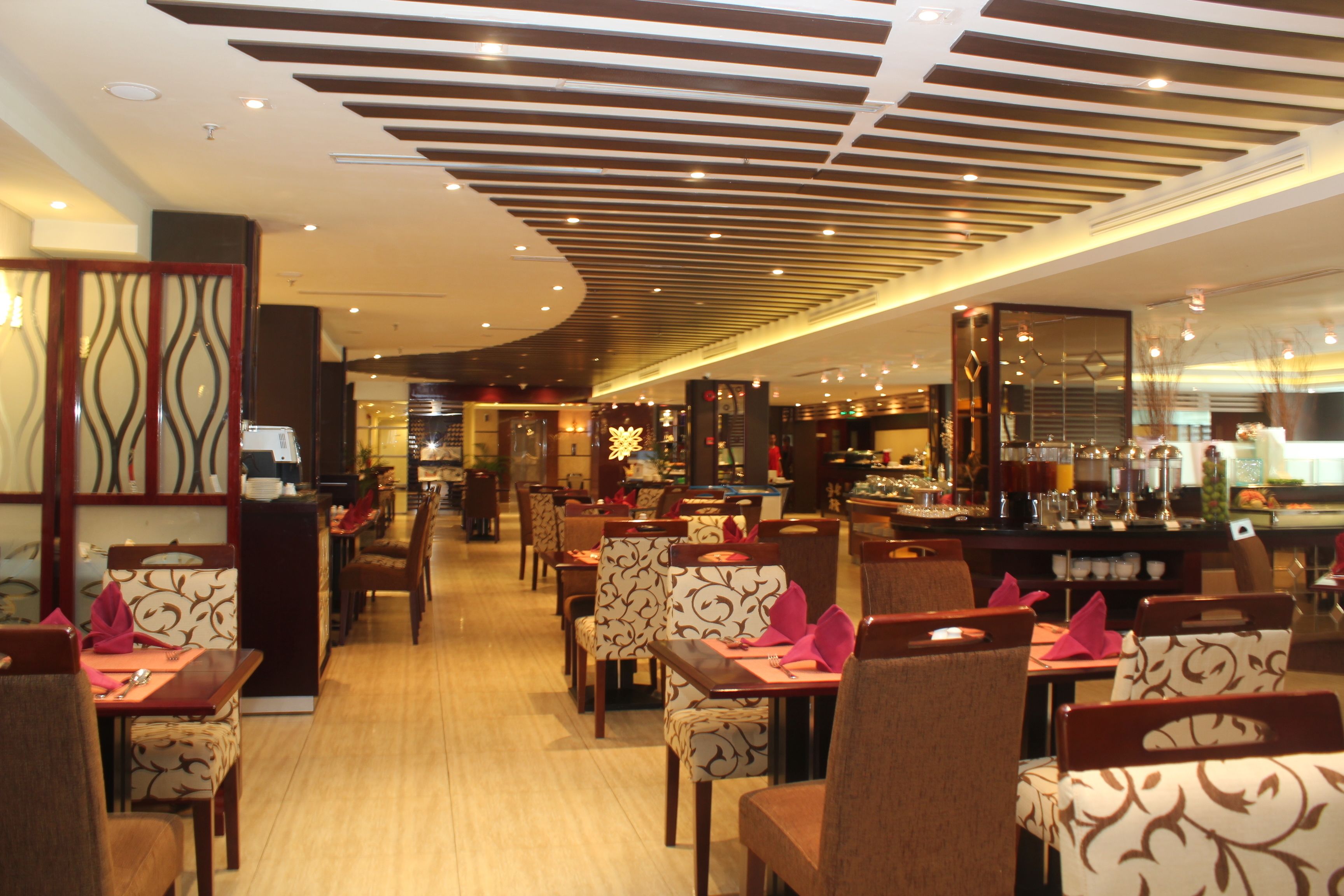 Un restaurante con mesas y sillas de madera, una zona de bar y un diseño de techo moderno.
