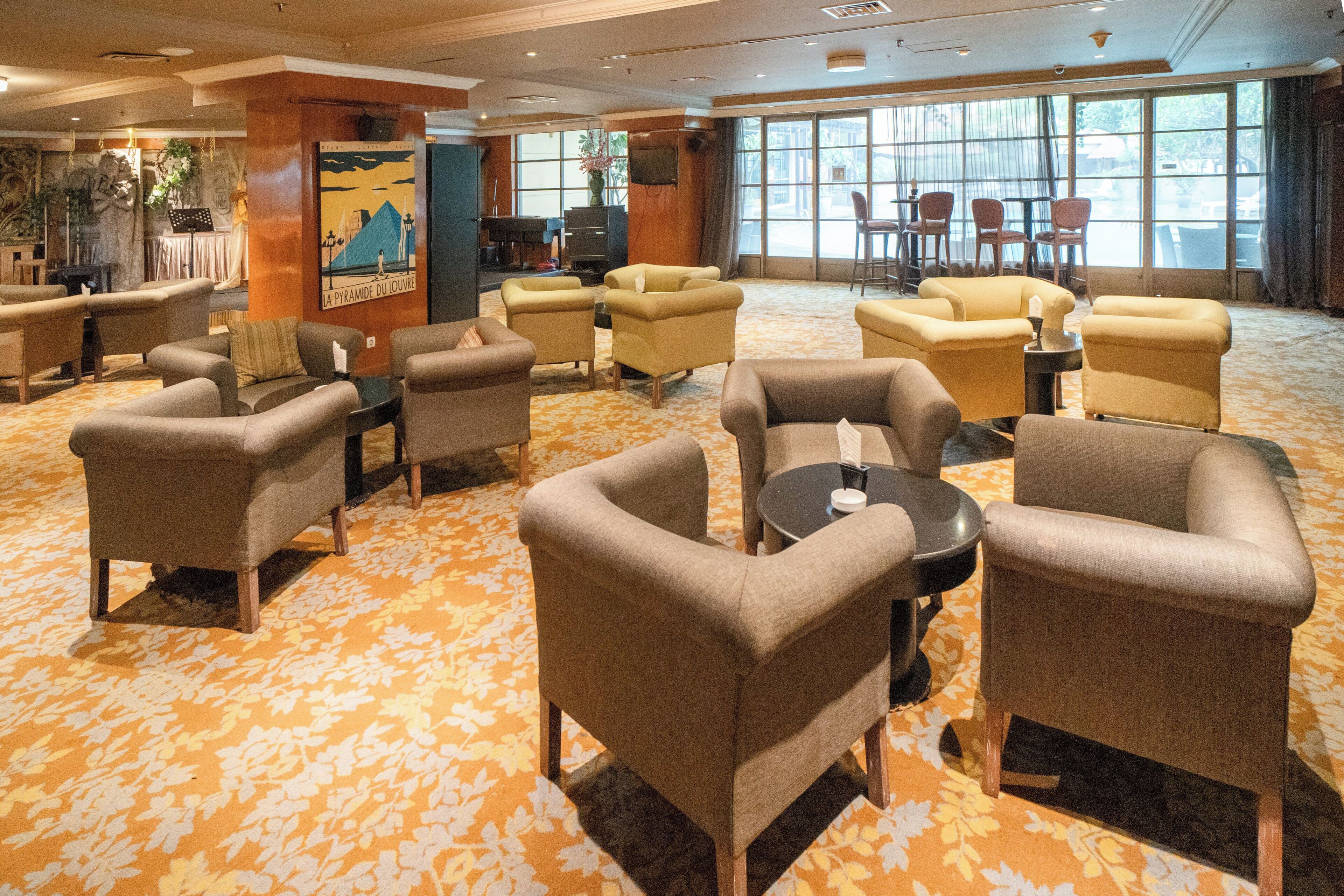 Un hall de hotel con varias zonas de estar, un piano y ventanas grandes.