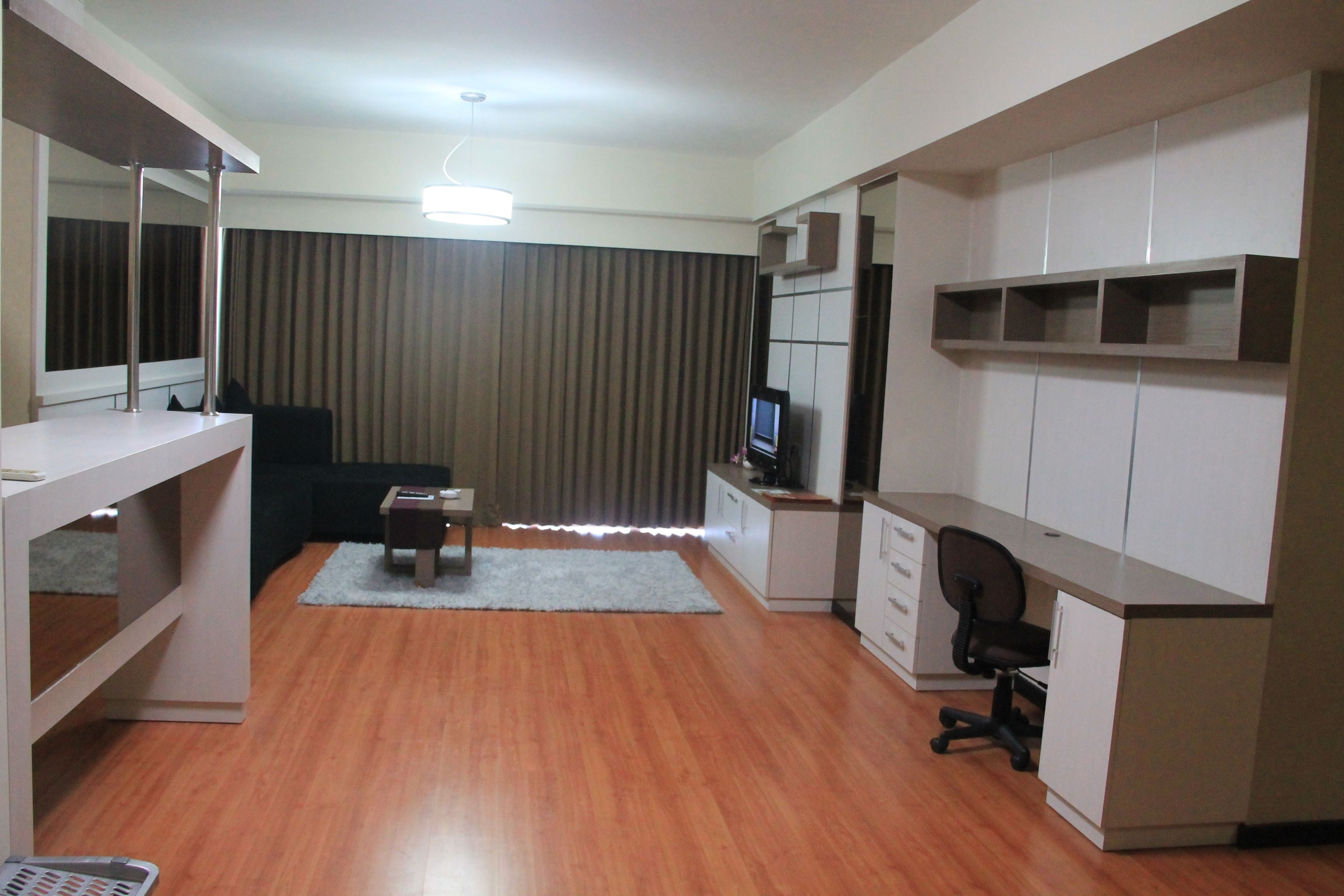 A compact hotel room with a wooden floor, a desk with a chair, a television, and a wardrobe.