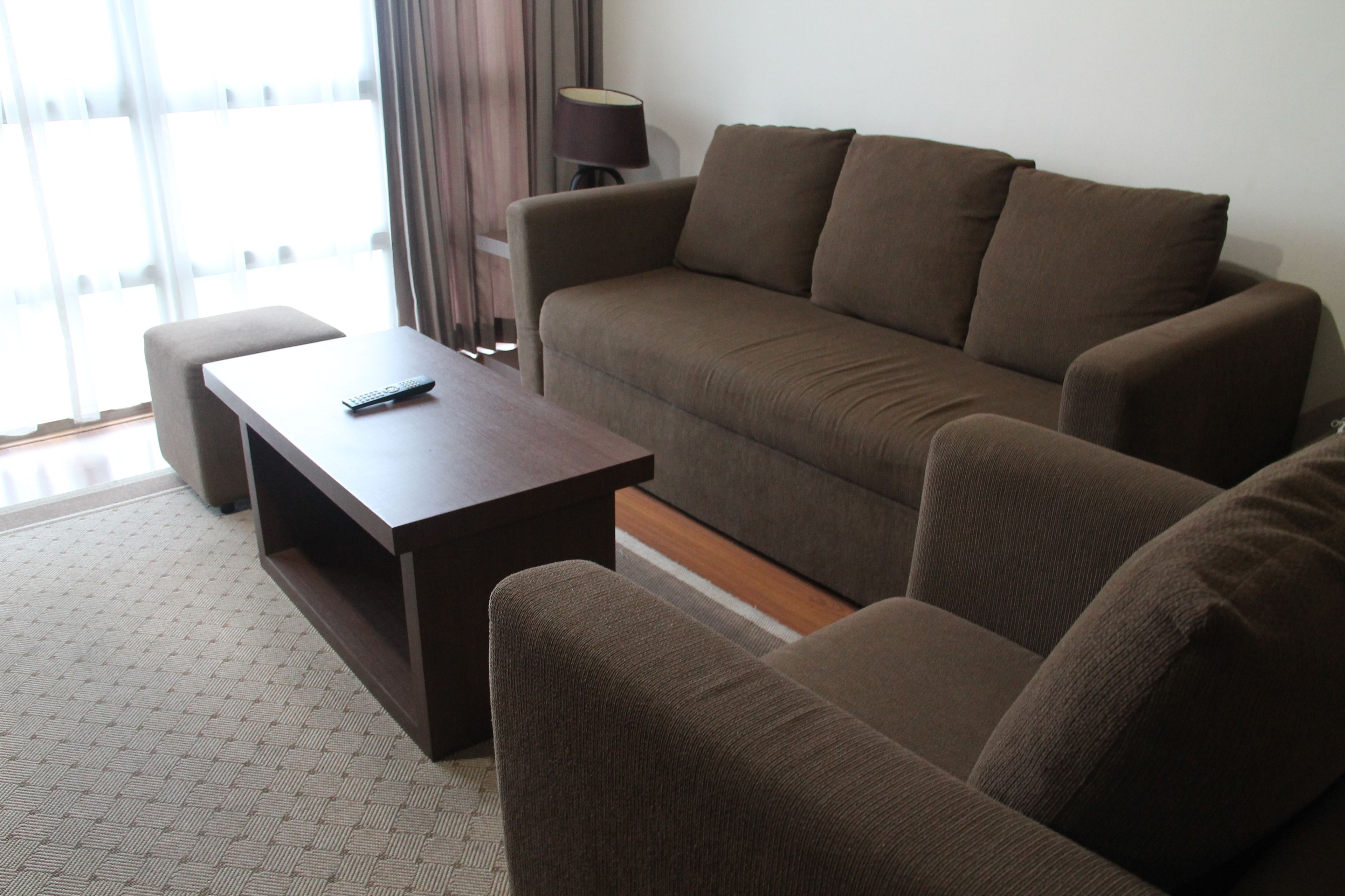 A living room with a brown sofa, a wooden coffee table, and a remote control on it.